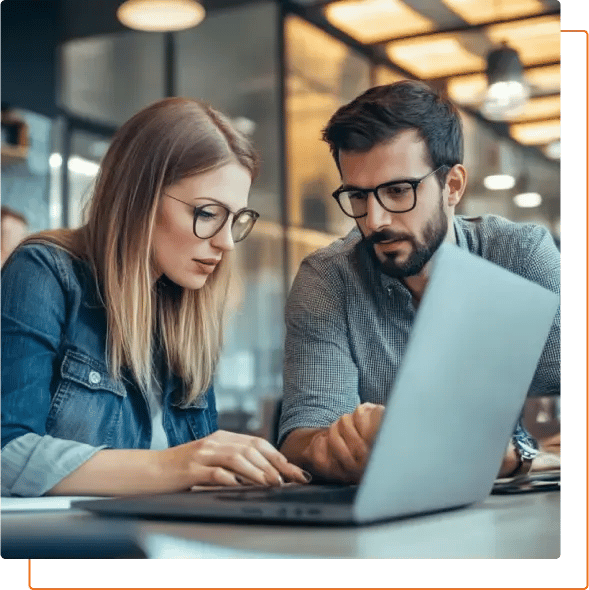 Two individuals collaborate over a laptop in a modern workspace, absorbed in their task amidst a stylish, well-lit environment.