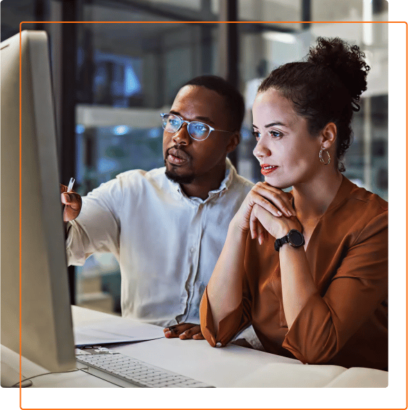 Two individuals focus intently on a computer screen in a modern office space, engaged in a discussion or brainstorming session.