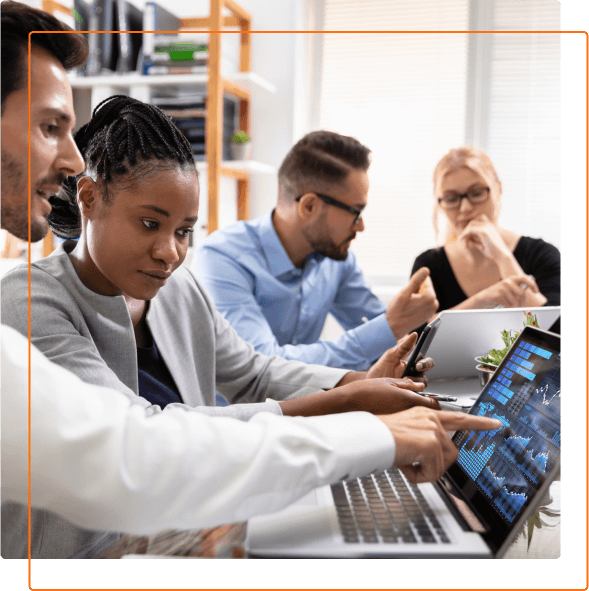 A diverse group of professionals collaborates around laptops, analyzing charts and data in a bright office setting.