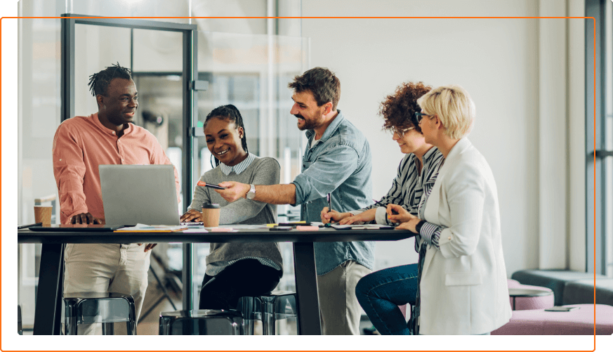 A diverse group of professionals collaborates around a table with a laptop and notes in a modern office environment.