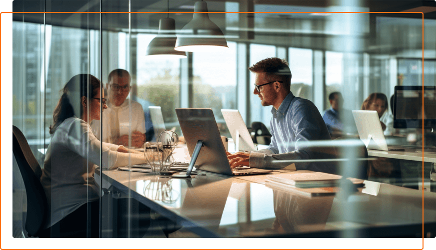 A modern office meeting with multiple individuals collaborating around a table, laptops opened, and a panoramic view outside.